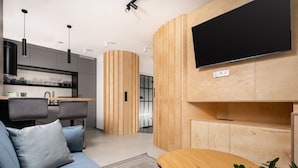 A modern living room with a sofa, a round wooden table, and a TV mounted on the wall. - Kalwaryjska Apartments (Kraków)