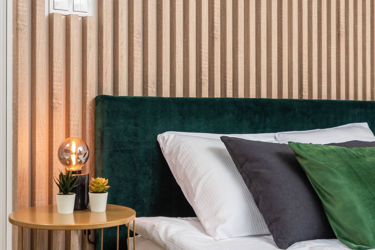 A neatly arranged bedroom with a green upholstered headboard, a round wooden side table with a globe lamp, and two potted plants.