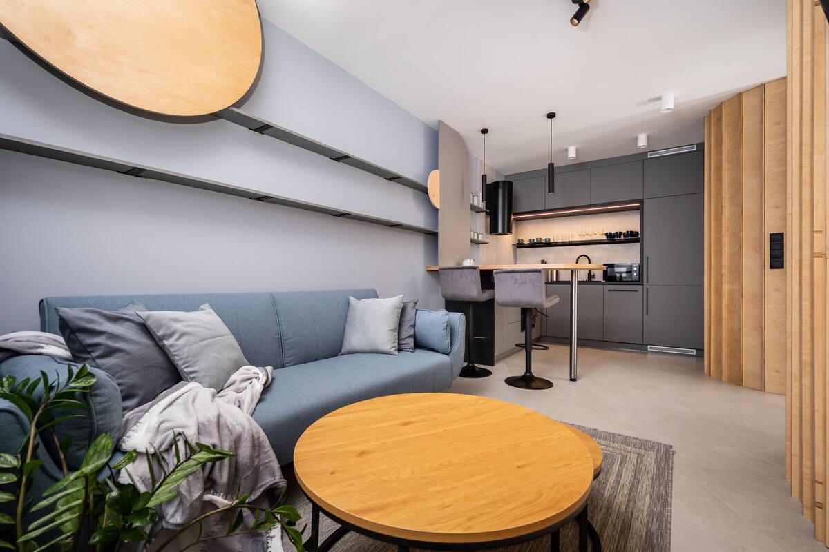 A modern living room with a sofa, a round wooden table, and a kitchen in the background.