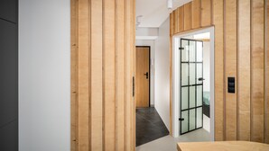 A modern hallway with wooden paneling, a glass door leading to a room, and a visible bed. - Kalwaryjska Apartments (Kraków)