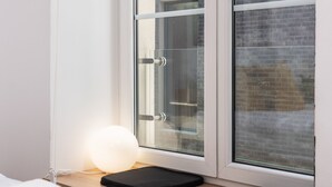 A room with a window, a bedside table with a lamp, and a bed with white bedding. - Kalwaryjska Apartments (Kraków)