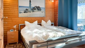 Une chambre avec un mur en bois, un lit avec une literie blanche, une table de chevet avec une lampe et un tableau représentant un phare.
