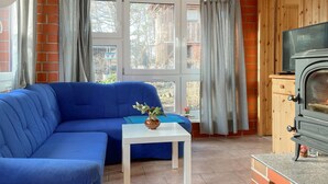 Un salon chaleureux avec un canapé bleu, une petite table blanche ornée d’un vase et un poêle à bois.