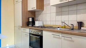 Une cuisine moderne avec des meubles blancs, un four en acier inoxydable, une machine à café et un évier doté d’un distributeur de savon.
