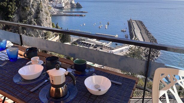 Una mesa con alimentos para el desayuno y vistas de un pueblo costero con edificios y barcos.