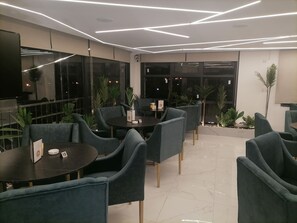 A modern indoor seating area with dark round tables and blue upholstered chairs, featuring a clean, contemporary design with geometric ceiling lighting. - Durrat al Israa Residence  (Amman)
