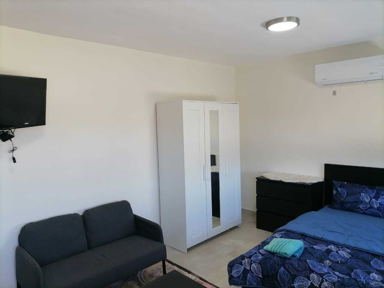 Un dormitorio con cama, armario, cómoda negra, televisor montado en la pared y equipo de aire acondicionado.