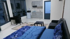 A modern bedroom with a large bed, a desk, a chair, and a small kitchenette.