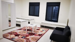 A living room with a sofa, a coffee table, a patterned rug, a wardrobe, and two windows.