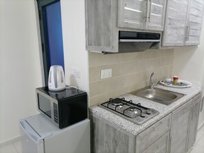 A compact kitchen with a microwave, kettle, gas stove, sink, and granite countertop. - Durrat al Israa Residence  (Amman)
