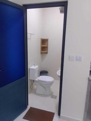 A bathroom with a white toilet, a small shelf, and a blue door. - Durrat al Israa Residence  (Amman)