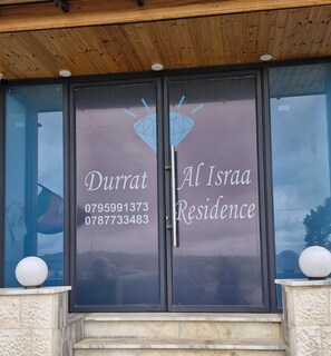 A building entrance with two glass doors displaying the name 'Durrat Al Israa Residence' and contact numbers. - Durrat al Israa Residence  (Amman)