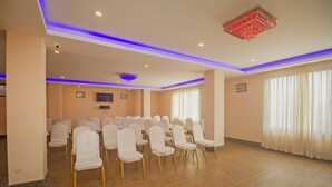 Un salón de conferencias con filas de sillas blancas, un techo con iluminación LED azul y un elemento decorativo luminoso rojo.