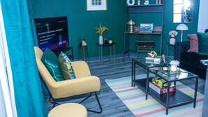 A living room with teal walls, a yellow armchair, a glass coffee table, and a television displaying an advertisement. - Dudley 3bedroom Home-perfect for Long & Short Stay (Dudley)