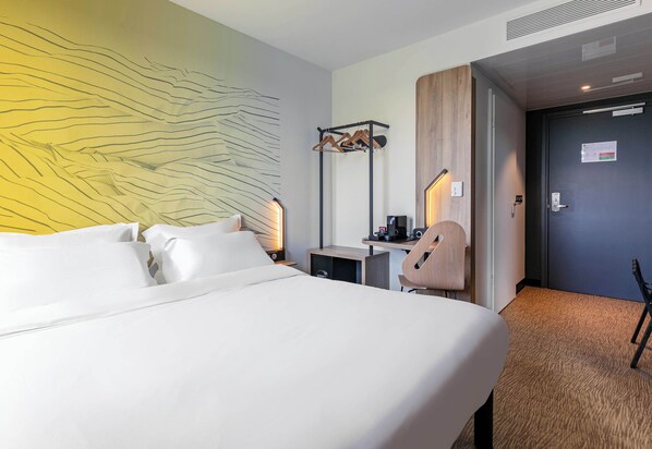 A hotel room with a large bed, a desk with a chair, a coat rack, and a wall art piece. - B&B Hotel Mulhouse Bâle Aéroport (Hésingue)