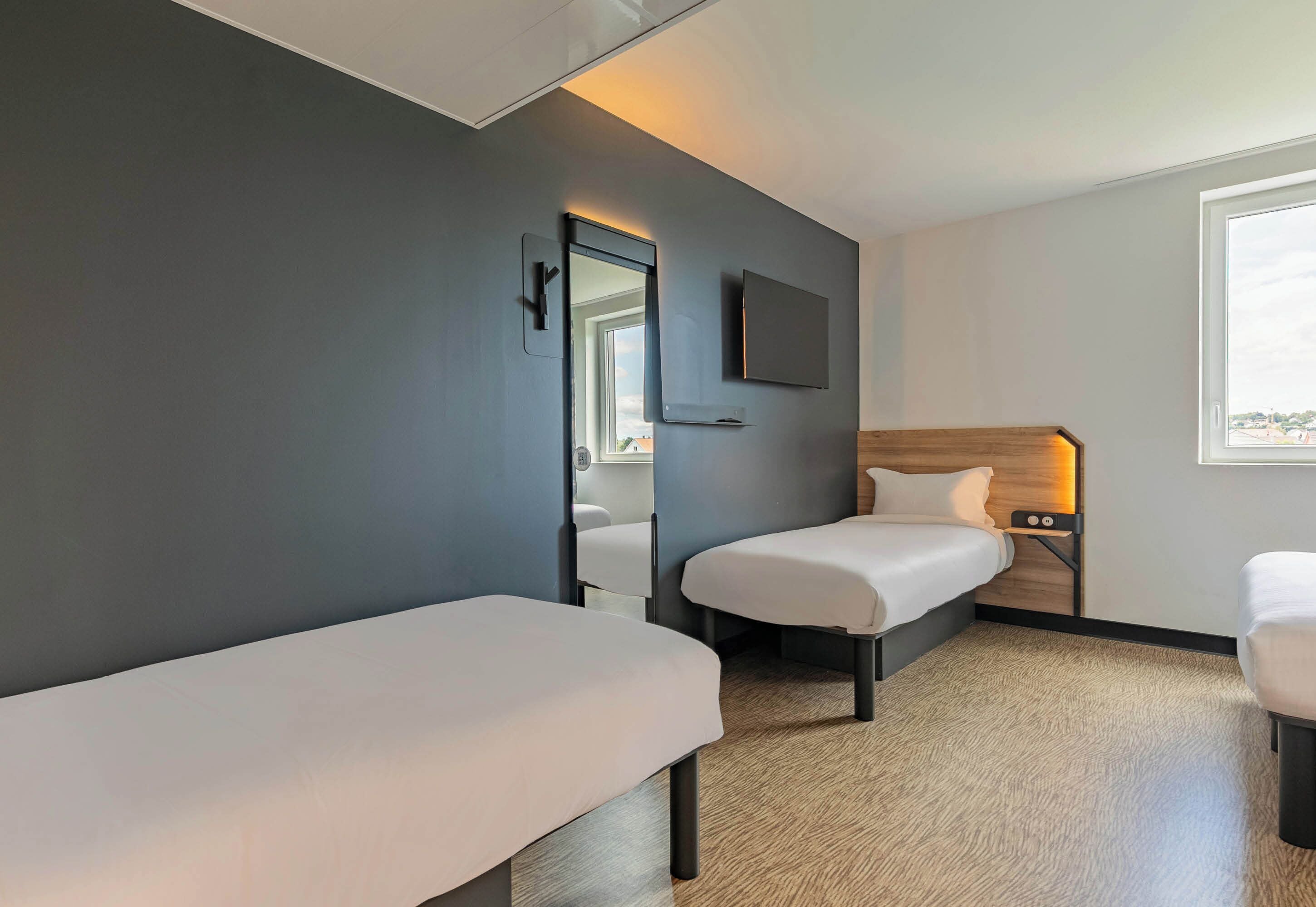 Een moderne hotelkamer met twee enkele bedden, een flatscreen televisie aan de muur en een raam met uitzicht op de stad.