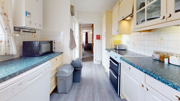A compact kitchen with a microwave, toaster, and oven. There is a trash bin and a small trash bag on the floor. The kitchen has white cabinets and a blue countertop. - 4 Bedroom Home - Sleeps 10 - Free Parking (Cambridge)