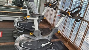 Tres bicicletas estáticas con la etiqueta MATRIX en un gimnasio que ofrece vistas de edificios a través de amplios ventanales.