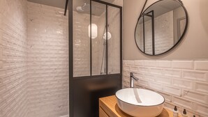 A modern bathroom with a glass-enclosed shower, a round mirror, and a wooden vanity with a large sink. - Appart'hôtel East Paris Suite (Paris)