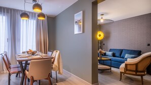 A modern living room with a dining area, featuring a blue sofa, wooden dining table, and pendant lighting. - Appart'hôtel East Paris Suite (Paris)