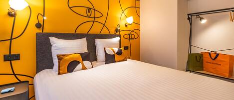 A hotel room with a bed, a nightstand, a wall-mounted lamp, and a luggage rack with bags.