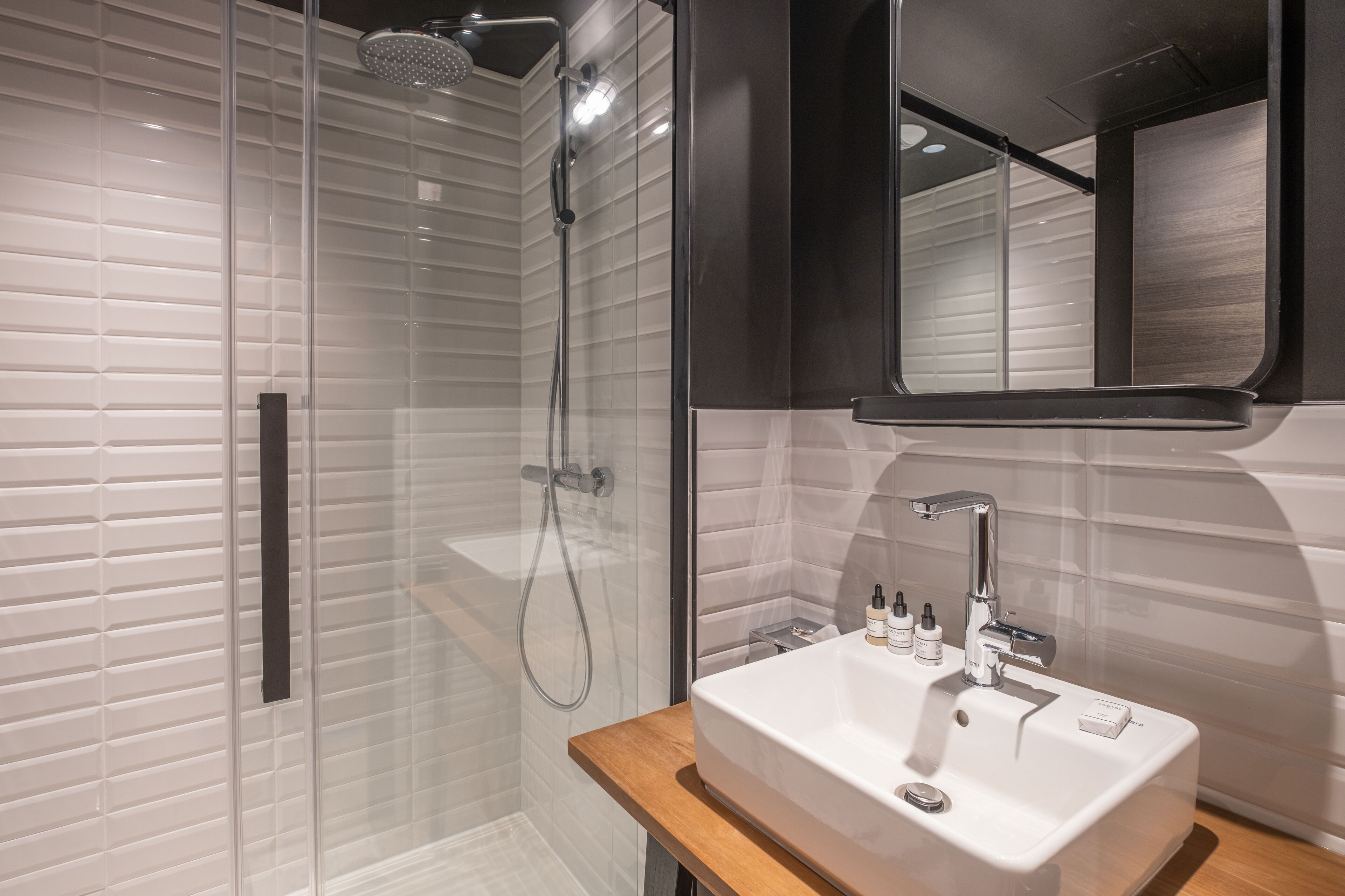 A modern bathroom with a glass-enclosed shower, a white sink with a wooden countertop, and a mirror above the sink.