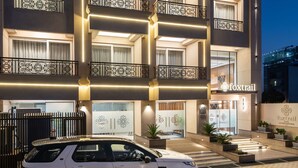 Ein mehrstöckiges Hotel mit moderner Fassade, ein weißer SUV vor dem Gebäude und ein gut beleuchteter Eingangsbereich.