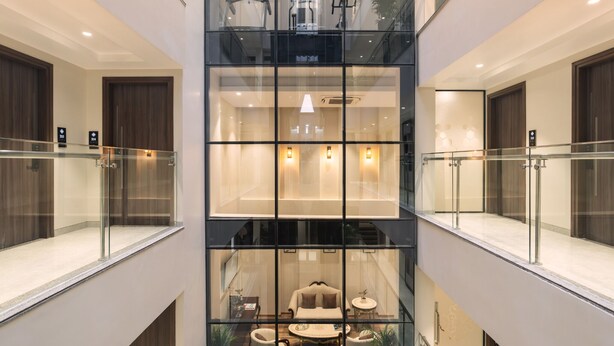 Eine moderne Hotelhalle mit einem Glasatrium, einer Sitzecke mit Sofa und Couchtisch sowie einer Treppe zu den oberen Etagen.