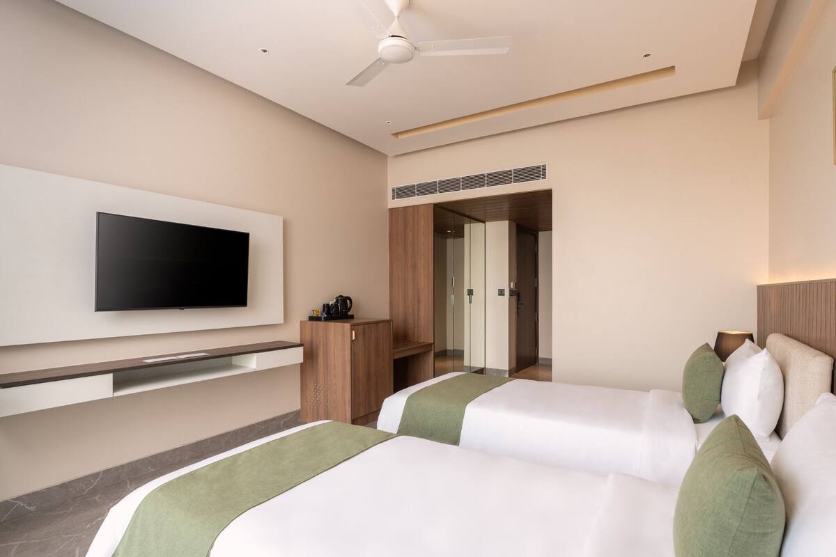 A hotel room with two beds, a flat-screen TV mounted on the wall, a ceiling fan, and a wooden cabinet.