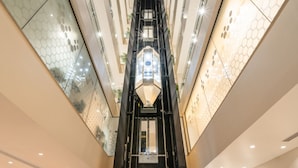 Ein modernes Interieur mit einem zentralen Aufzugsschacht, Glaswänden und einem geometrischen Muster an der Decke.