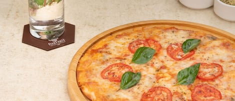 A pizza with tomato slices and basil leaves on a wooden board.