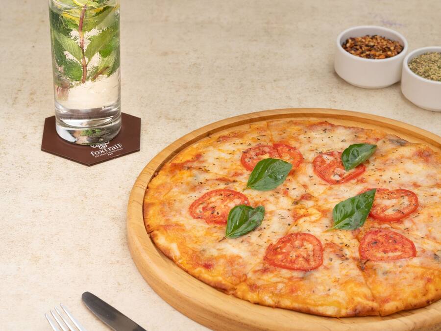 A pizza with tomato slices and basil leaves on a wooden board.