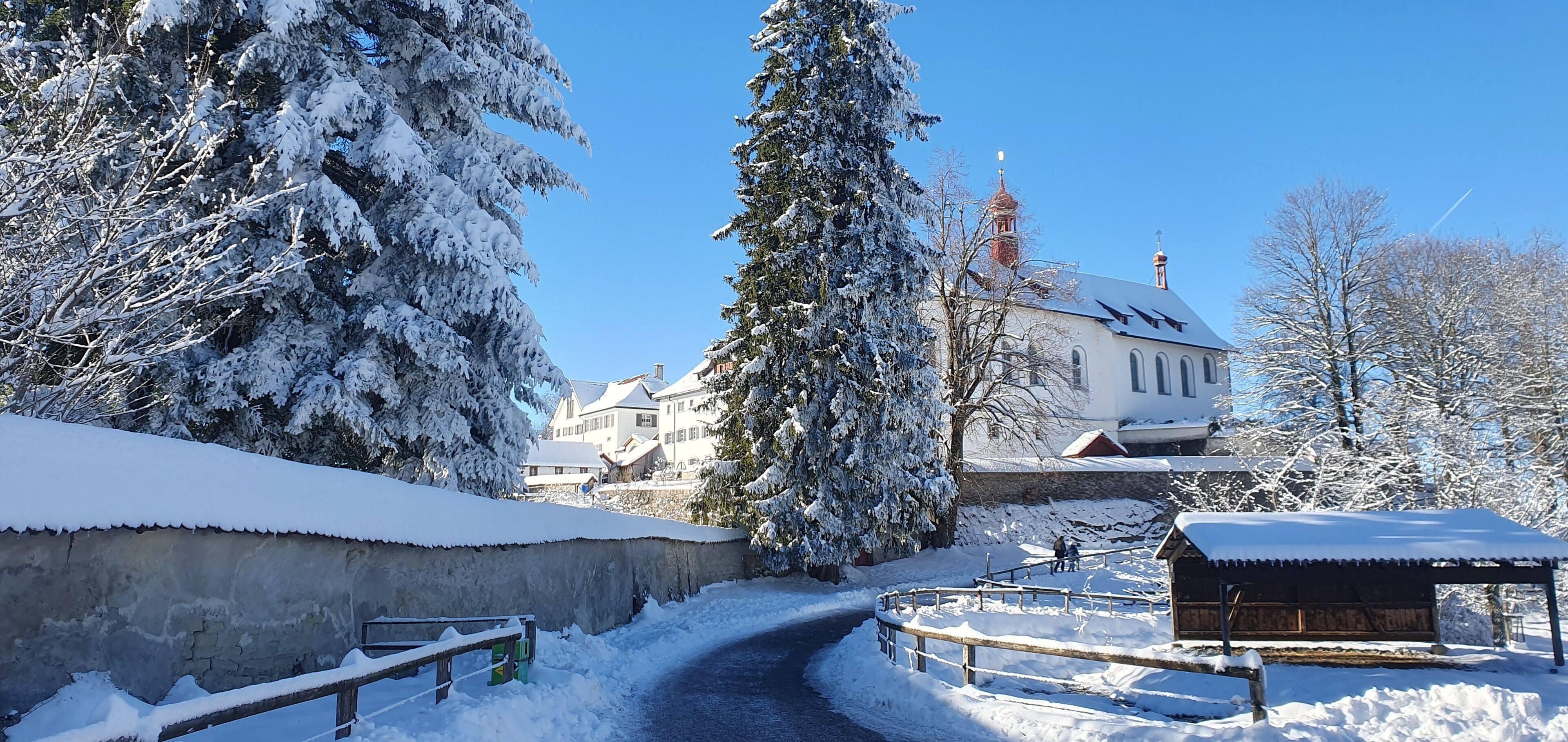 Paisagem coberta de neve com uma igreja, um banco de madeira e um caminho.