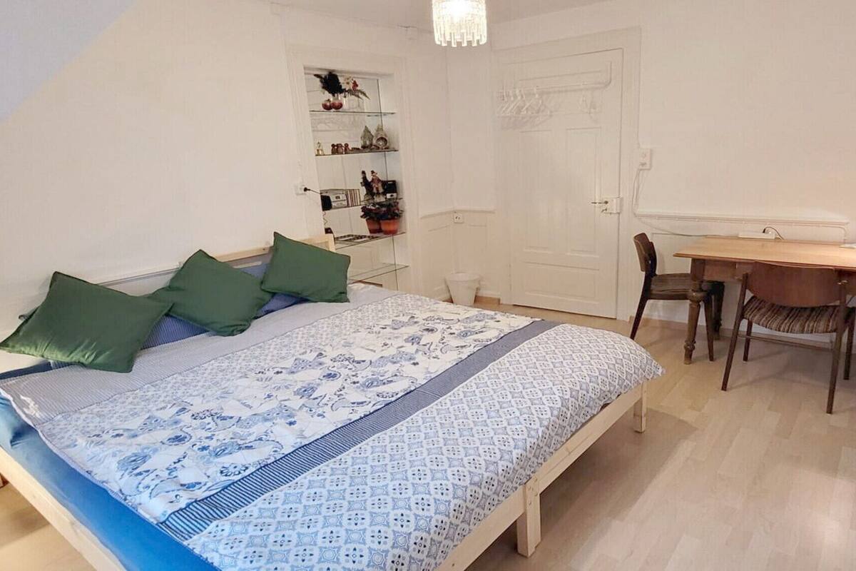 A bedroom with a bed, a desk, a chair, and a shelf with decorative items.