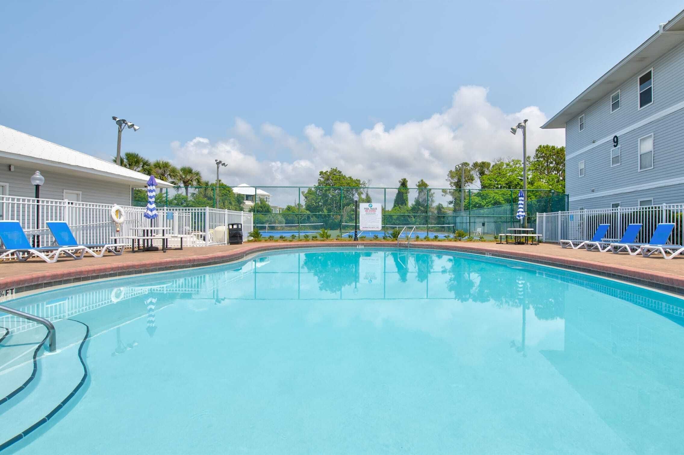 Une piscine avec des chaises longues, une clôture et un bâtiment en arrière-plan.