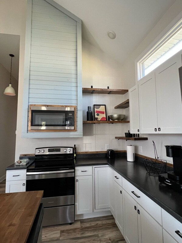 A modern kitchen with white cabinets, a stainless steel stove, a microwave, and a wooden countertop. - This bungalow is a 2 bedroom(s), 2 bathrooms, located in Gas City, IN. (Gas City)