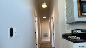 A narrow hallway with wooden flooring, white walls, and a ceiling light fixture.