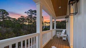 A wooden deck with white railings and two white chairs, overlooking a forested area. - New 4BR Home | Pool | Elevator | 8 Bikes (Rosemary Beach)