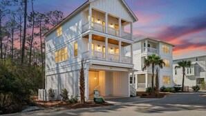 A two-story white building with a balcony on the upper floor, surrounded by trees and a sunset sky. - New 4BR Home | Pool | Elevator | 8 Bikes (Rosemary Beach)