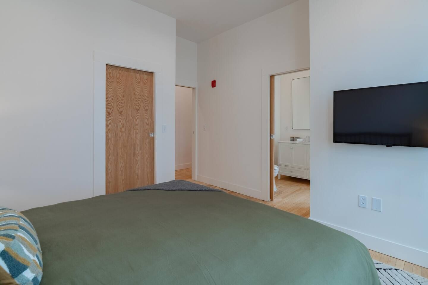 Una camera da letto con un letto, una televisione montata a parete e una porta in legno.
