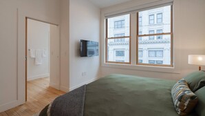 Ein Schlafzimmer mit großem Fenster, Flachbildfernseher und einem Bett mit grüner Bettwäsche.