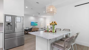 A modern kitchen with a central island, stainless steel appliances, and a dining area with wicker chairs. - Heart of Rosemary & Alys | 2 Masters | Sleeps 16 (Watersound)