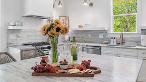 A modern kitchen with a marble countertop, a built-in stove, and a large window with a view of trees. - Heart of Rosemary & Alys | 2 Masters | Sleeps 16 (Watersound)