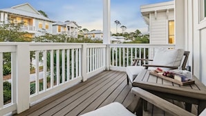A covered outdoor area with a wooden deck, white railings, and a table with a cushion and food items. - Heart of Rosemary & Alys | 2 Masters | Sleeps 16 (Watersound)