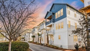 A row of two-story houses with balconies, a paved driveway, and a tree-lined street. - Heart of Rosemary & Alys | 2 Masters | Sleeps 16 (Watersound)