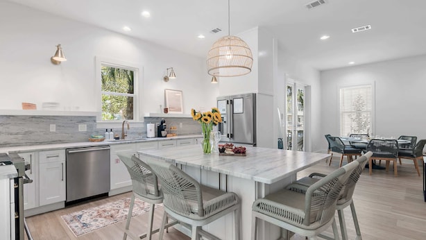 A modern kitchen with a central island, stainless steel appliances, and a dining area with a table and chairs. - Heart of Rosemary & Alys | 2 Masters | Sleeps 16 (Watersound)