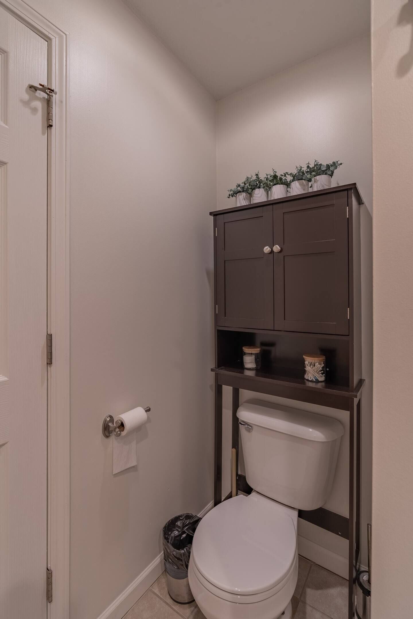 Un baño pequeño con un inodoro, un mueble sobre el inodoro y un cubo de basura.