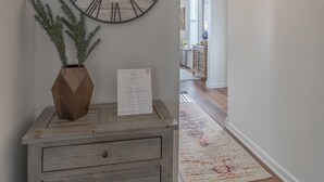 Een hal met een houten dressoir, een grote wandklok en een potplant.