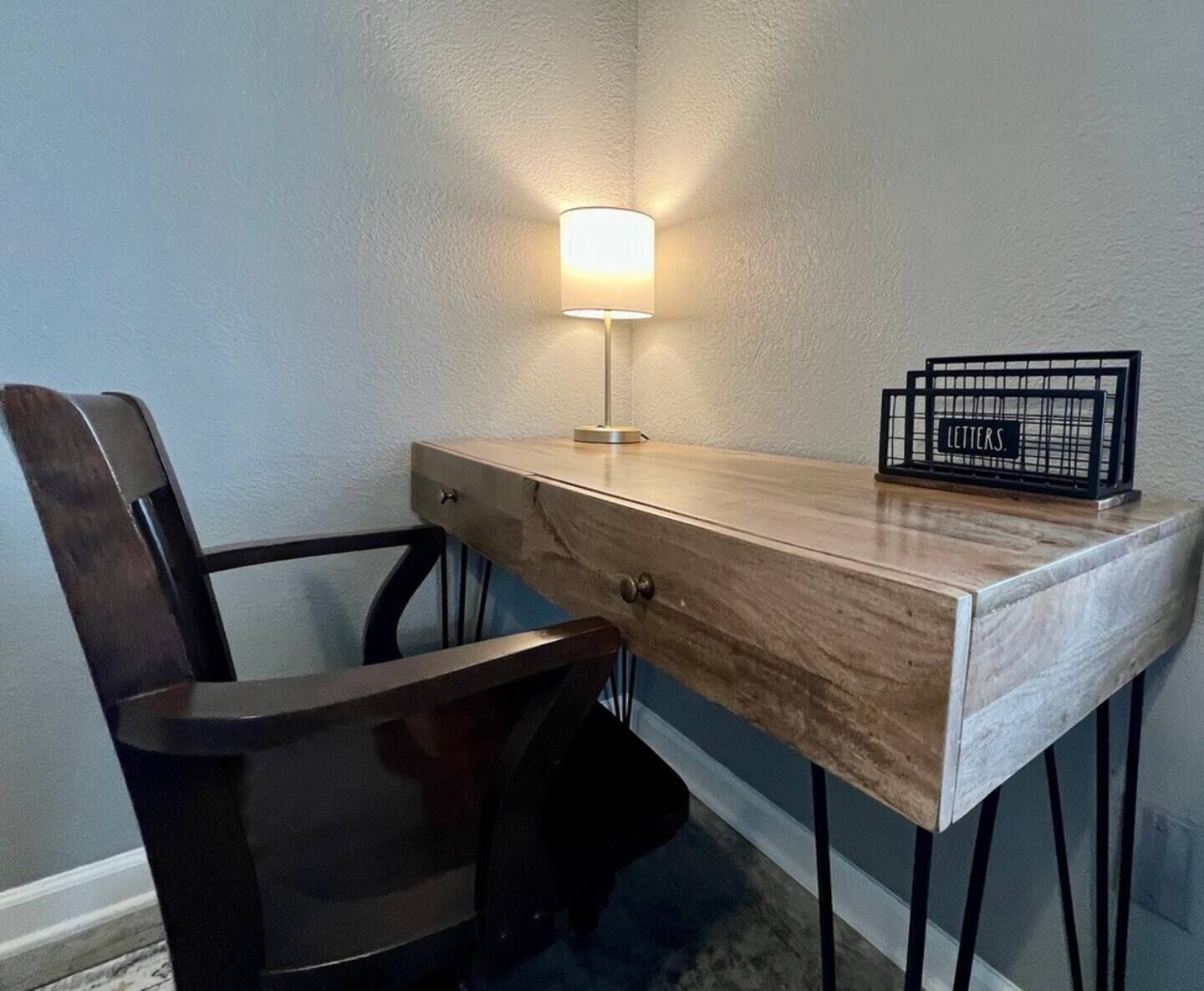 Un bureau d’angle avec une lampe, une chaise et un présentoir à lettres.