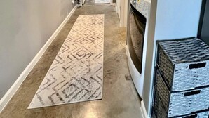 A hallway with a patterned rug, a washing machine, and stacked crates.